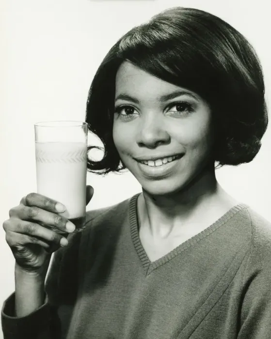 Framed Print : Young woman holding glass of milk in studio, smiling, (B&W), portrait