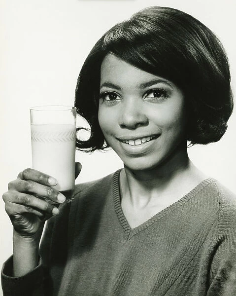Young woman holding glass of milk in studio, smiling, (B&W), portrait