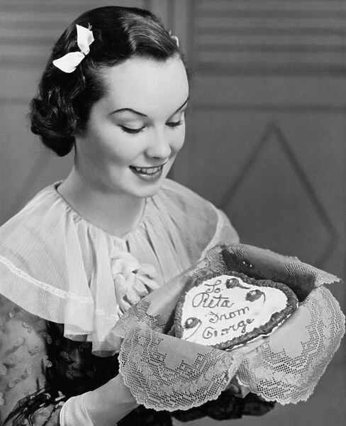 Young woman holding heart-shaped cake, (B&W)