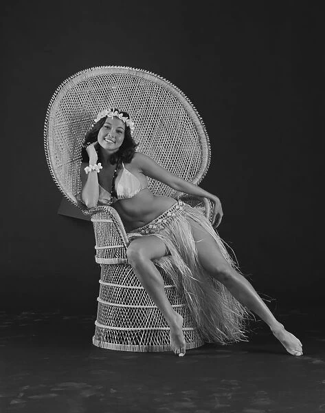 Young woman hula dancer in traditional clothing sitting on wicker chair, smiling, portrait