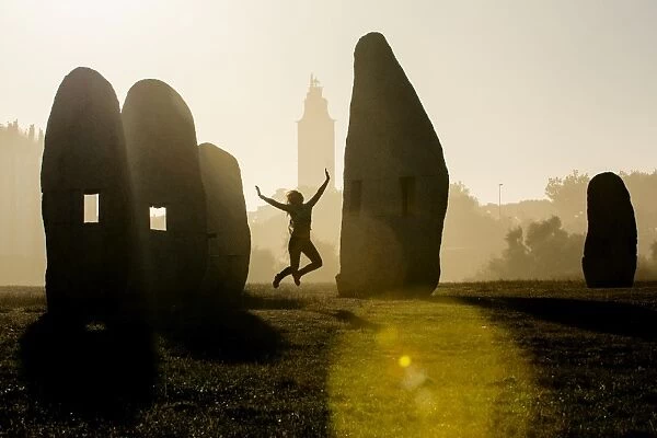 Young woman jumping in midair outdoors, in front of Hercules Tower, A Coruna, Spain