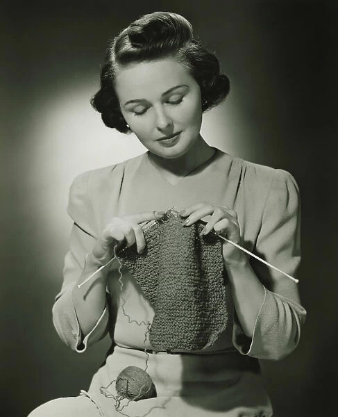 Young woman knitting in studio, (B&W)