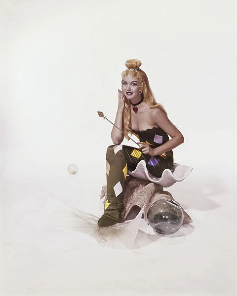 Young woman in mermaid costume sitting on shell, smiling, portrait