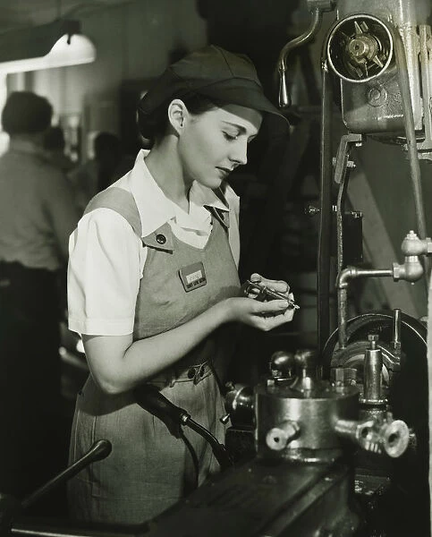 Young woman in overalls working by lathe in factory, (B&W)