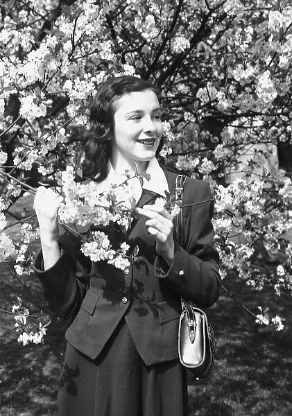 Young woman posing by blooming tree in park, (B&W), portrait