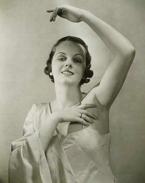 Young woman raising hand, posing in studio, (B&W), portrait