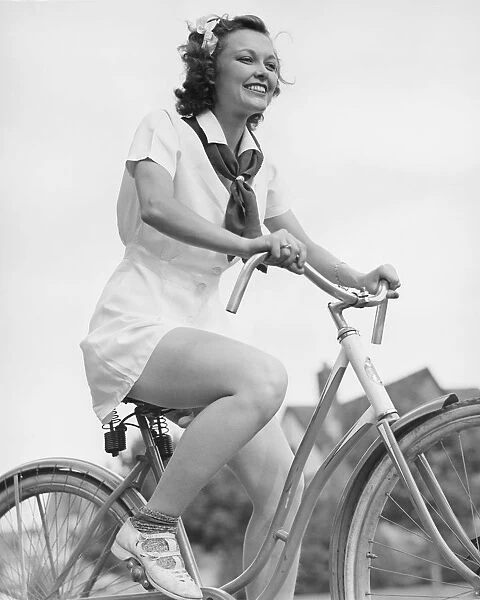 Young woman riding bicycle, (B&W), low angle view