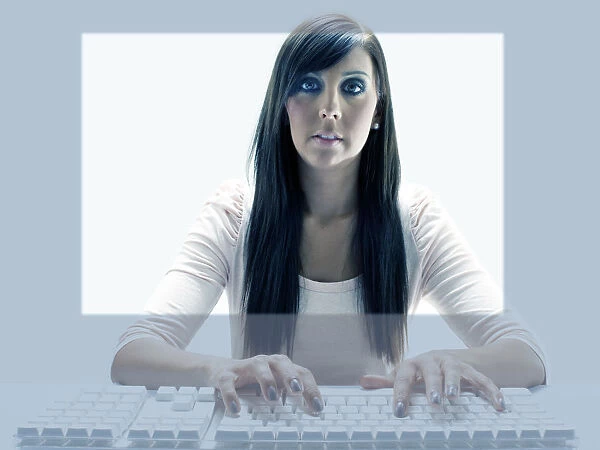 Young woman seen through the display of a computer while using the keyboard
