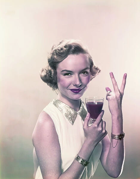 Young woman showing v sign with wine glass, smiling, portrait