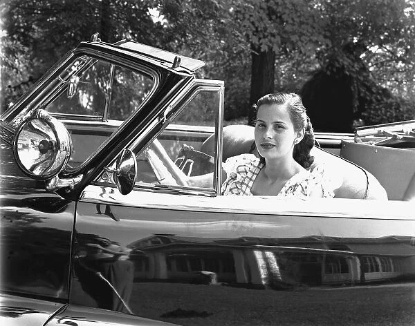 Young woman sitting in convertible car, (B&W), portrait