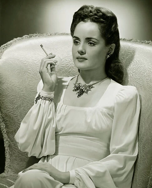 Young woman sitting in stylish armchair, smoking, (B&W)