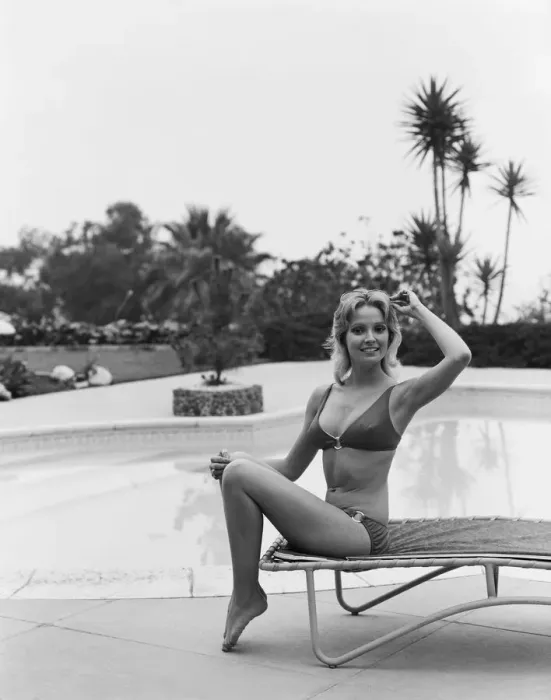 Framed Print : Young woman sitting on sun lounger by swimming pool, smiling, portrait Framed Print : Young woman sitting on sun lounger by swimming pool, smiling, portrait
