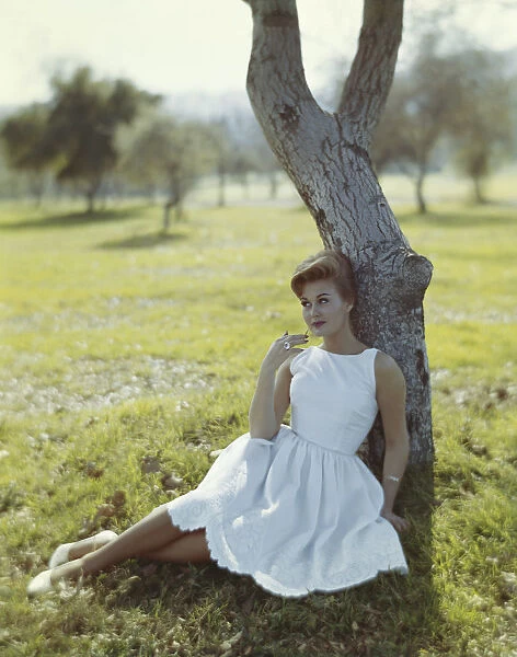 Young woman sitting against tree trunk