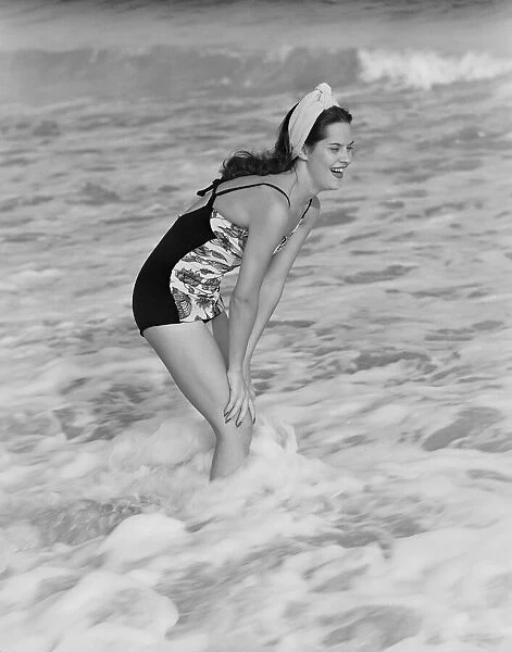 A young woman stands laughing in the surf, circa 1960. (Photo by H