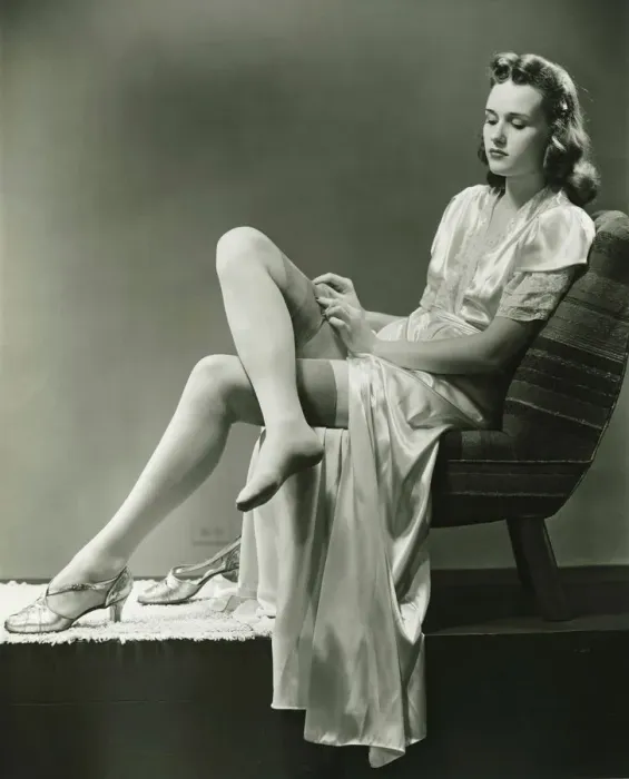 Framed Print : Young woman straightening stockings, sitting on chair in studio, (B&W) Framed Print : Young woman straightening stockings, sitting on chair in studio, (B&W)