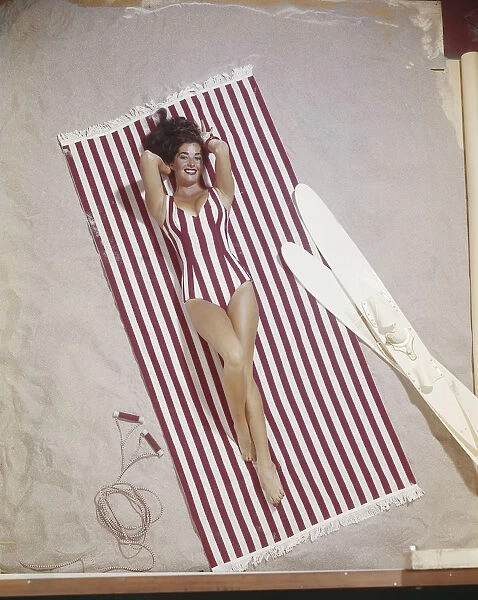 Young woman in striped swimwear lying on striped blanket