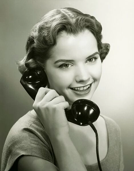 Young woman talking on phone in studio, (B&W), portrait