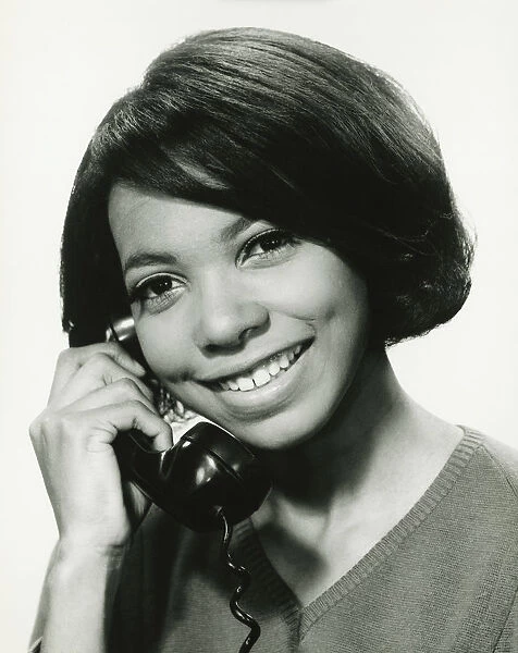 Young woman using phone in studio, smiling, (B&W), portrait