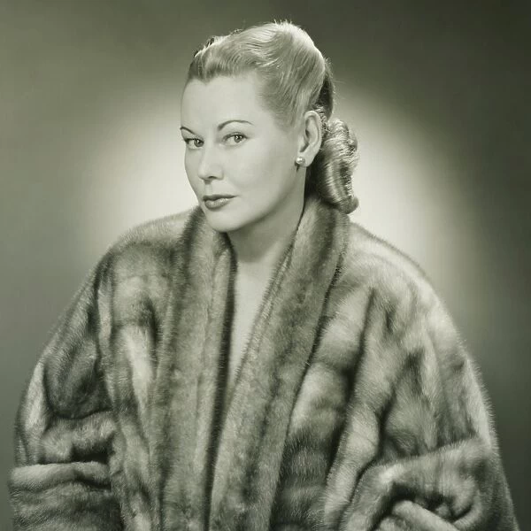 Young woman wearing fur coat in studio, (B&W), portrait