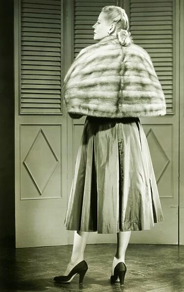 Young woman wearing fur standing in empty room, (B&W)