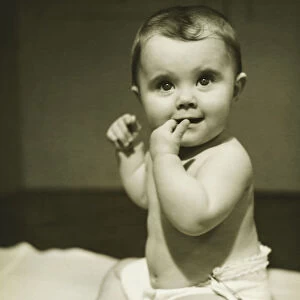 Baby boy (12-18 months) sitting on bedspread, sucking finger, (B&W), close-up
