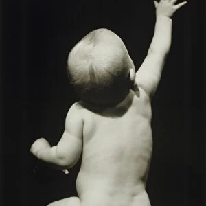 Baby boy (6-12 months) raising hand sitting in studio, (B&W)