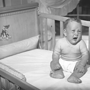 Baby boy (6-9 months) sitting in crib, crying, (B&W)