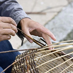 A basket weaver sitting on the street and weaving a basket, Brittany, France, Europe