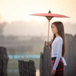 Femme belle tenant une parapluie traditionnel rouge et marchant sur le pont U Bein, Myanmar. Femme belle tenant une parapluie traditionnel rouge et marchant sur le pont U Bein, Myanmar.