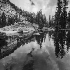 Black and white image of granite outcropping with boulders by lake, Yosemite National Park, California, USA