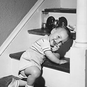 Boy (18-24 months) kneeling on steps, smiling, (B&W)