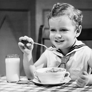 Boy (4-5) wearing sailor suit, eating at table, (B&W), portrait