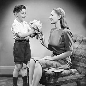 Boy (8-9) giving bunch of flowers to mother (B&W)