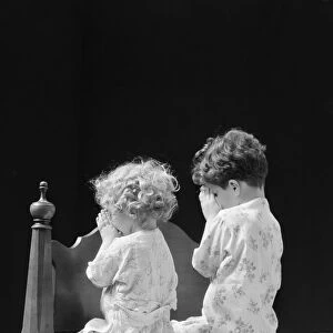 Boy and girl kneeling by bed praying, rear view