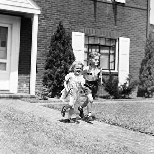 Boy and girl running down sidewalk, holding school books, going to school
