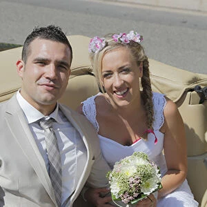 Bride and groom posing in the back seat of an open car, convertible