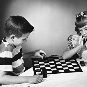 Brother and sister playing checkers at table