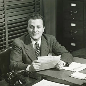 Businessman holding documents, sitting at office, (B&W)
