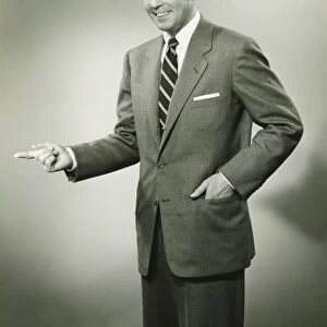 Businessman pointing sideways in studio, smiling, (B&W), portrait