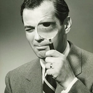 Businessman in full suit in studio looking through magnifying glass, (B&W), portrait