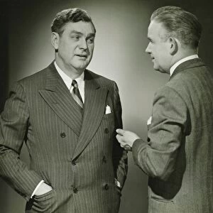 Two businessmen talking in studio, (B&W), portrait