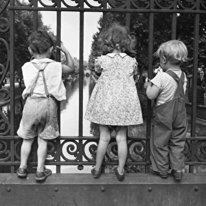 Three children peer through the fence on a bridge over one of Londons many canals