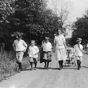 Country Walk; group of seven children walking in a row, and an eighth being pulled in a cart