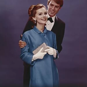 Couple in formal clothing standing against blue background, smiling