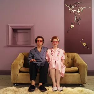Couple side by side on sofa wearing pink tinted glasses, portrait