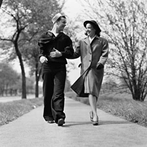 Couple walking arm in arm outdoors, man wearing naval sailor uniform, woman wearing coat