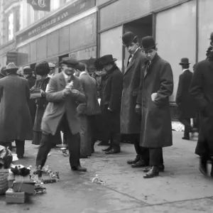 A crowd on a sidewalk observes street peddlers selling toys A crowd on a sidewalk observes street peddlers selling toys