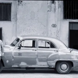 Cuban man leaning against car smoking cigar (B&W)