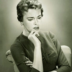 Distraught woman sitting in armchair in studio, (B&W), portrait