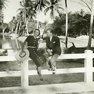 Elegant couple sitting on fence in tropical environment, (B&W)